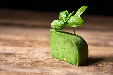 Image showing A piece of gourmet basil cheese with twig of basil on rough wooden planks