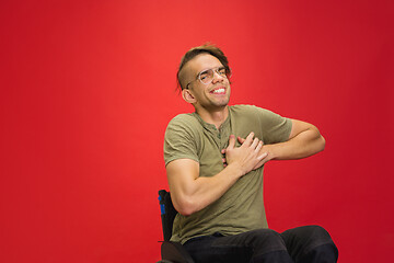 Image showing Caucasian young man\'s portrait isolated on red studio background. Human emotions concept