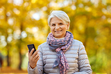 Image showing happy senior woman with smartphone at autumn park