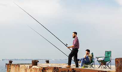 Image showing male friends with fishing rods on sea pier