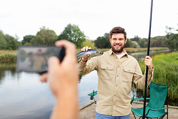 Image showing friend photographing fisherman with fish at lake