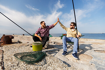 Image showing male friends with fishing rods making high five