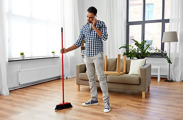 Image showing man with broom cleaning and calling on smartphone