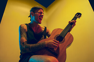 Image showing Young caucasian musician inspired performing on yellow background in neon light