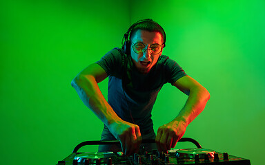 Image showing Young caucasian musician in headphones performing on green background in neon light