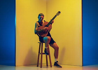 Image showing Young caucasian musician inspired performing on yellow background in neon light