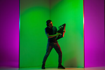 Image showing Young caucasian musician in headphones performing on bicolored green-purple background in neon light