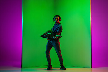 Image showing Young caucasian musician in headphones performing on bicolored green-purple background in neon light