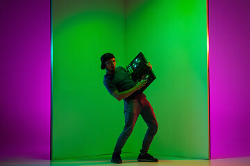 Image showing Young caucasian musician in headphones performing on bicolored green-purple background in neon light