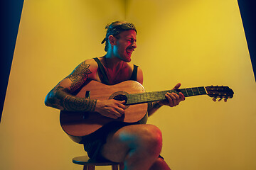 Image showing Young caucasian musician inspired performing on yellow background in neon light