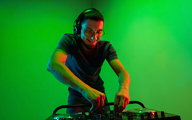 Image showing Young caucasian musician in headphones performing on green background in neon light