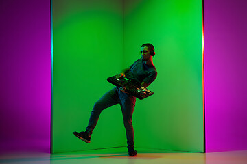 Image showing Young caucasian musician in headphones performing on bicolored green-purple background in neon light