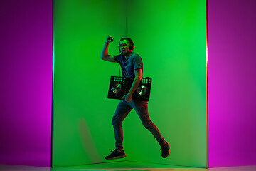 Image showing Young caucasian musician in headphones performing on bicolored green-purple background in neon light