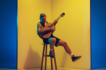 Image showing Young caucasian musician inspired performing on yellow background in neon light