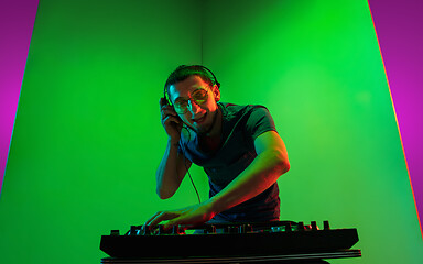 Image showing Young caucasian musician in headphones performing on bicolored green-purple background in neon light