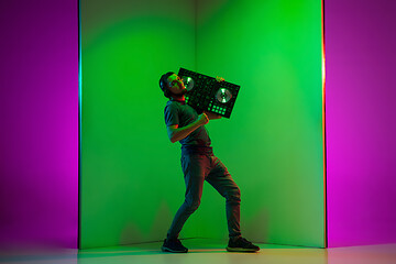 Image showing Young caucasian musician in headphones performing on bicolored green-purple background in neon light