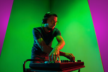 Image showing Young caucasian musician in headphones performing on bicolored green-purple background in neon light