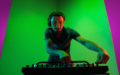 Image showing Young caucasian musician in headphones performing on bicolored green-purple background in neon light