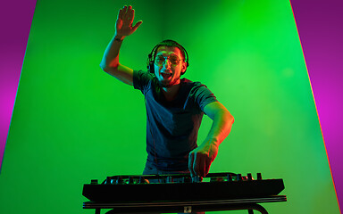 Image showing Young caucasian musician in headphones performing on bicolored green-purple background in neon light