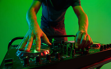 Image showing Young caucasian musician in headphones performing on green background in neon light
