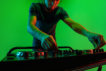 Image showing Young caucasian musician in headphones performing on green background in neon light