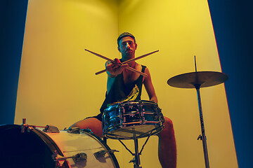 Image showing Young caucasian musician inspired performing on yellow background in neon light