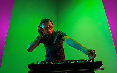 Image showing Young caucasian musician in headphones performing on bicolored green-purple background in neon light