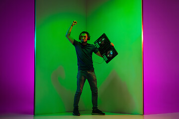 Image showing Young caucasian musician in headphones performing on bicolored green-purple background in neon light