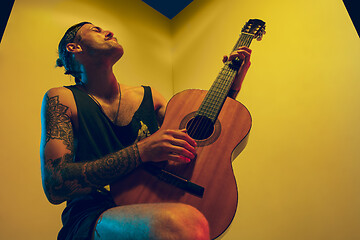 Image showing Young caucasian musician inspired performing on yellow background in neon light