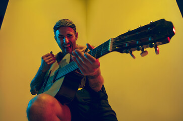 Image showing Young caucasian musician inspired performing on yellow background in neon light