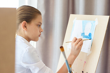 Image showing A girl in light clothes sits in front of an easel and draws still life