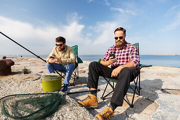 Image showing friends with smartphones fishing on pier at sea