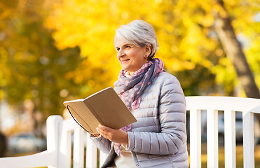 Image showing happy senior woman reading diary at autumn park