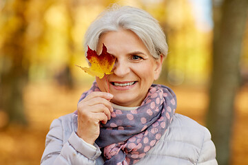 Image showing happy senior woman with maple leaf at autumn park