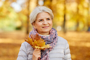 Image showing senior woman with maple leaves at autumn park