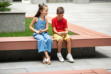 Image showing Two smiling kids, boy and girl playing smartphone together in town, city in summer day