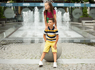Image showing Two smiling kids, boy and girl running together in town, city in summer day