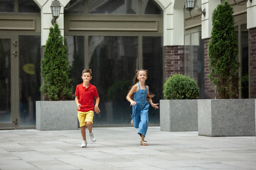 Image showing Two smiling kids, boy and girl running together in town, city in summer day