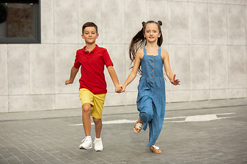 Image showing Two smiling kids, boy and girl running together in town, city in summer day