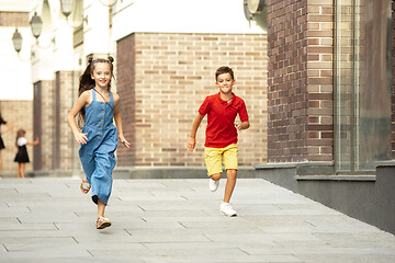 Image showing Two smiling kids, boy and girl running together in town, city in summer day