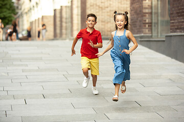 Image showing Two smiling kids, boy and girl running together in town, city in summer day