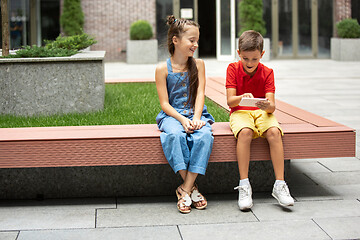 Image showing Two smiling kids, boy and girl playing smartphone together in town, city in summer day