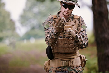 Image showing soldier preparing tactical and commpunication gear for action ba