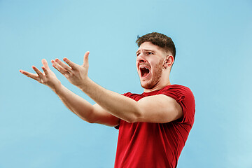 Image showing The young emotional angry man screaming on blue studio background