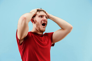 Image showing The young emotional angry man screaming on blue studio background