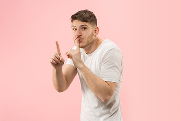 Image showing The young man whispering a secret behind her hand over pink background