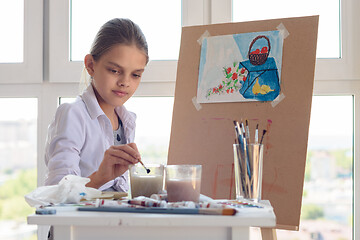 Image showing girl sits behind an easel and washes her brush in a glass of water