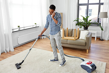 Image showing man with vacuum cleaner calling on cell at home