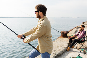 Image showing male friends with fishing rods on sea pier