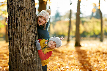 Image showing happy children peeking out tree at autumn park